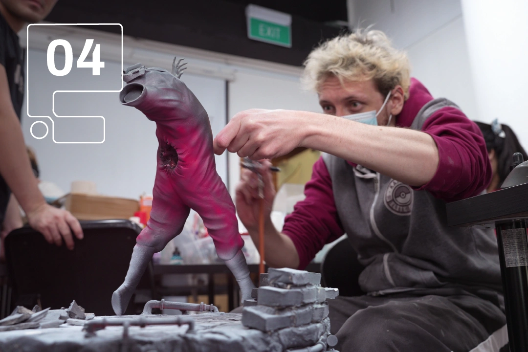 An artist meticulously paints a vibrant, humanoid sculpture, focusing on details and colors within a creative workspace.