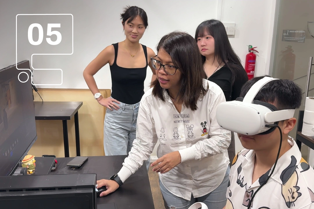 A group of individuals gather around a computer desk, with one person wearing a VR headset, engaged in a digital experience.