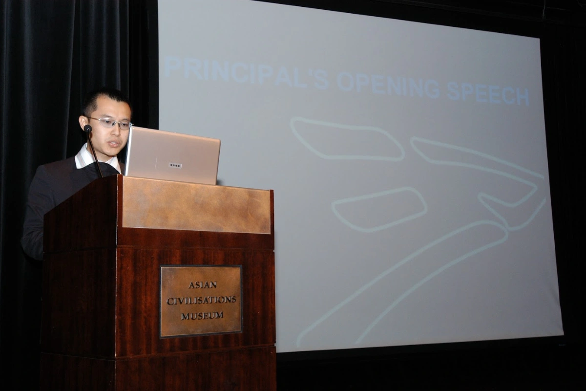 An archival photograph from the school's early years: a speaker at a lectern with a presentation projected behind him.