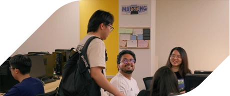 A group of students engage in conversation while surrounded by computers in a vibrant study space with colorful decor.